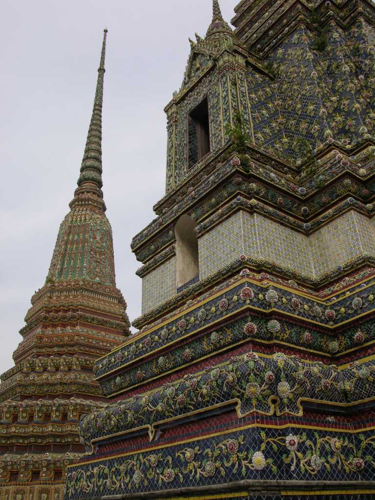 Bangkok 03 04 Wat Po Chedi Next to the Reclining Buddha wiharn is an enclosure holding the four largest of the temple's 95 chedis, each 42m high. All of the chedi at Wat Po are square, rather than the round bell shape generally preferred at the time. They are decorated with ceramic tiles and three dimensional ceramic pieces which form intricate floral patterns. The centre of the three chedi in a line is the oldest, having been built by Rama I to hold the Phra Si Sanphet Buddha image bought from Ayuthaya. Later, Rama III built the chedi north of this to hold the ashes of Rama II, and the one to the south to hold his own remains. The fourth chedi was built by Rama IV for unknown purposes.